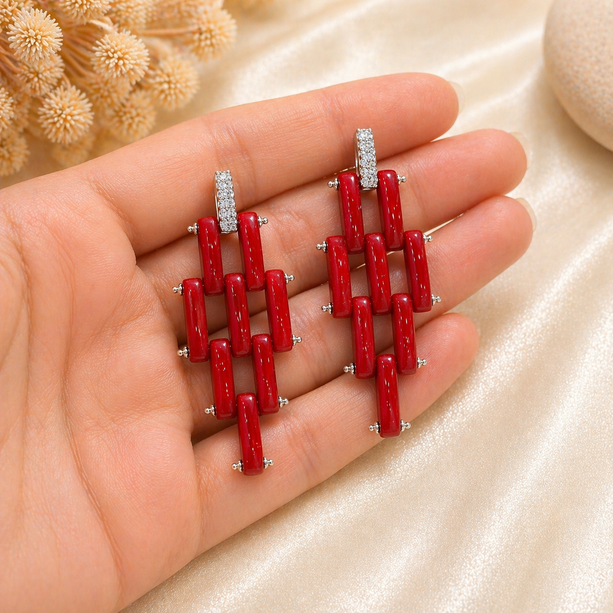 Orecchini modello Cartier in Argento 925 rodiato con fascette di Corallo Rosso Naturale del Mediterraneo e pavé di zirconi, mostrati nella mano per evidenziarne dimensioni e dettagli.