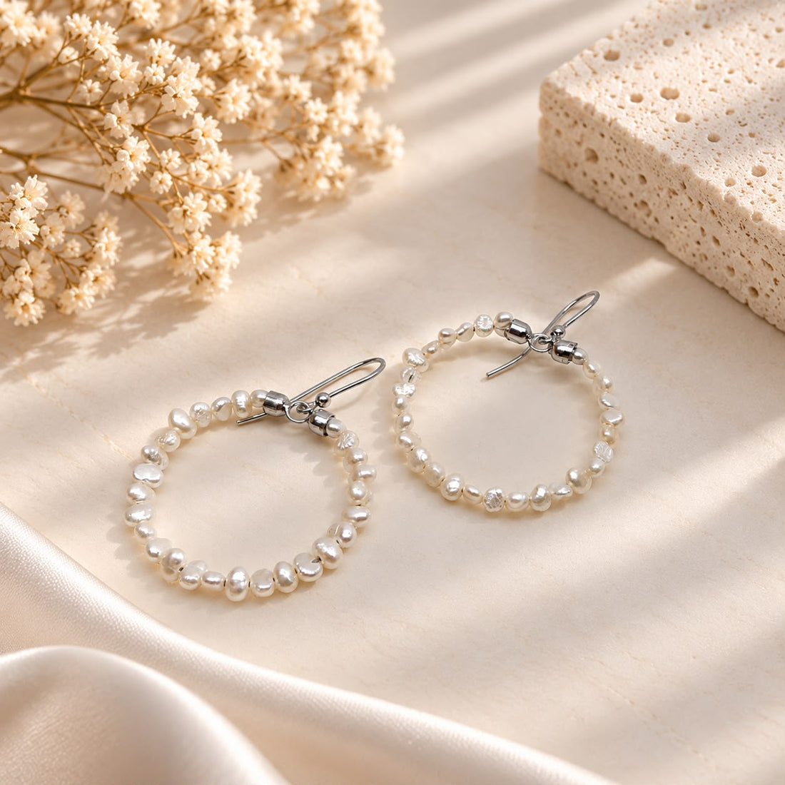 Orecchini a cerchio in Argento 925 rodiato con piccole perle barocche naturali d'acqua dolce, vista frontale su sfondo crema elegante.
