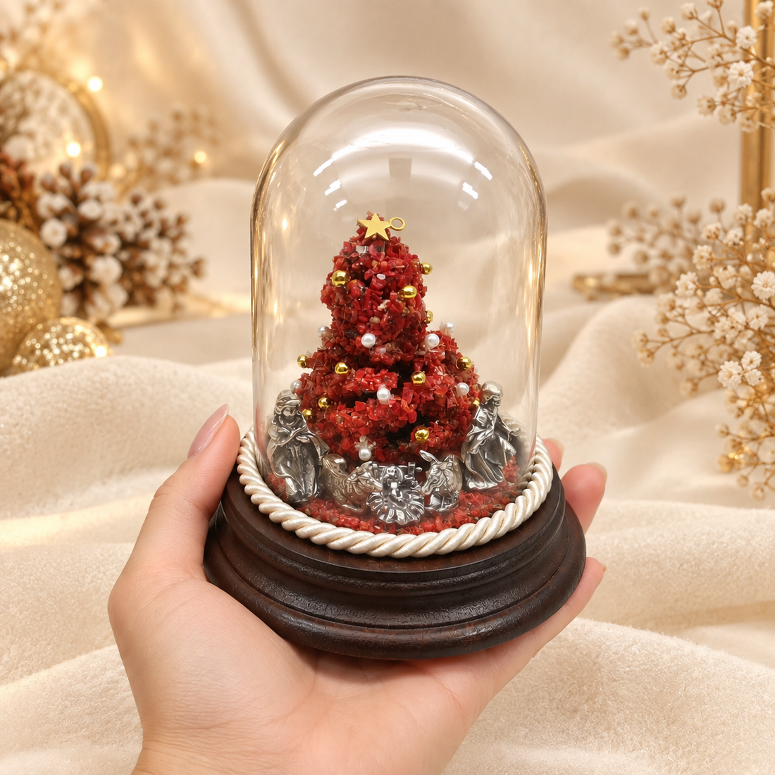 Presepe artigianale con albero in corallo rosso e Natività argentata sotto cupola di vetro, mostrato in mano per evidenziarne le dimensioni.
